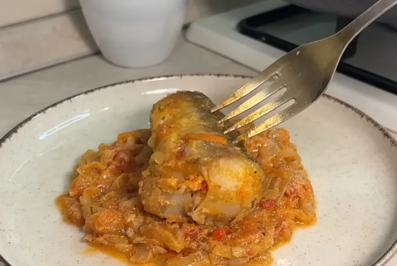 Золотистые кусочки хека, тушенные в густом сметанно-томатном соусе с луком и морковью